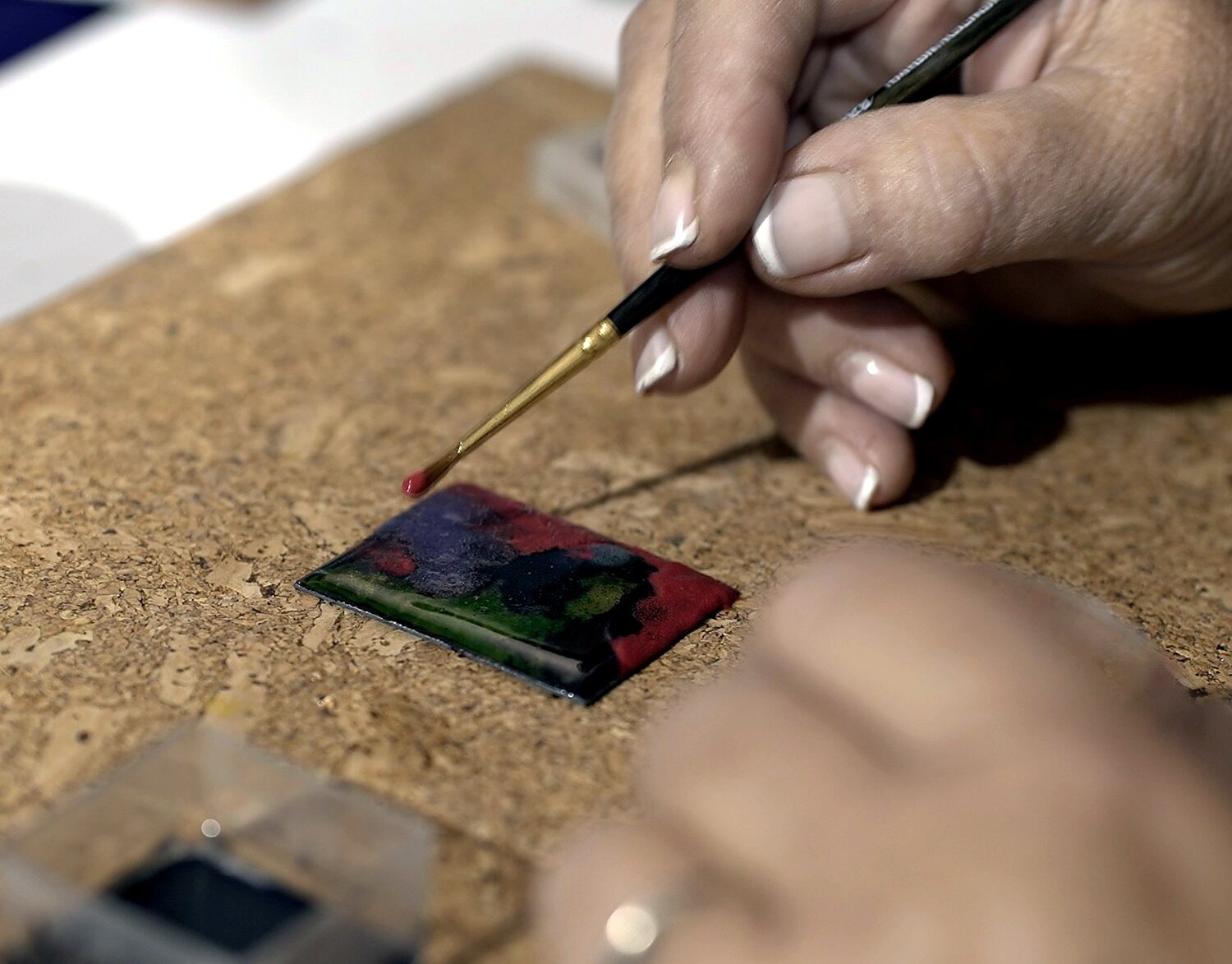 Mano pintando el detalle de una pieza de esmalte